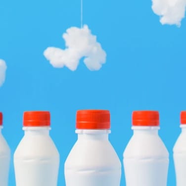 three milk bottles with red caps aligned next with each other with a blue sky that has white clouds background